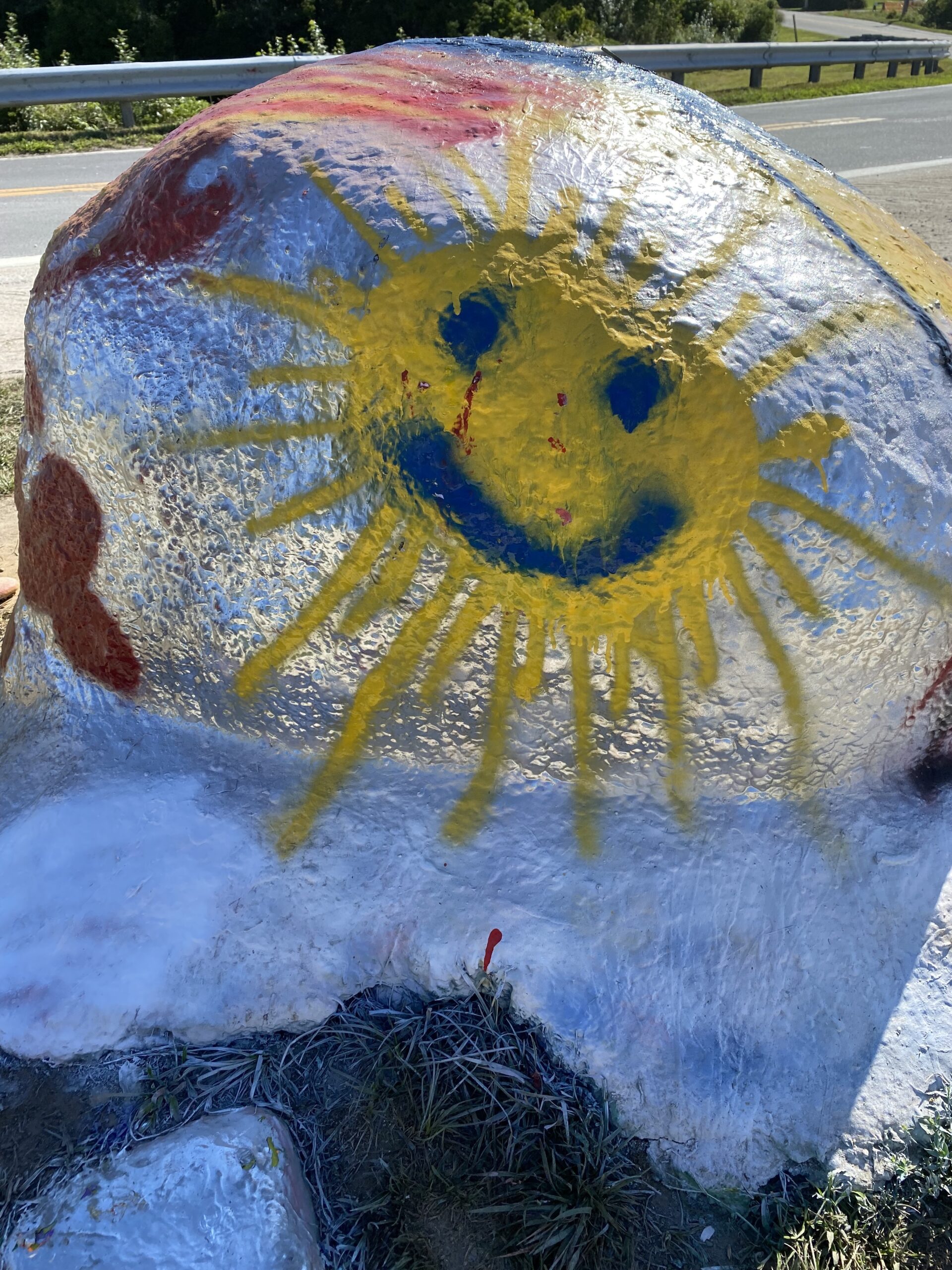 large boulder painted with a bright yellow smiley face in the shape of the sun