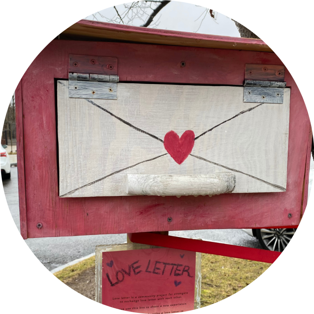 a photograph of a pink and white wooden mail box with an image of a white envelope and a red heart painted on it